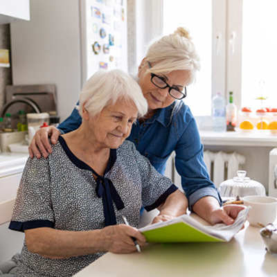 Afbeelding van 2 vrouwen. De ene vrouw ondersteunt de andere bij het lezen van een boek.