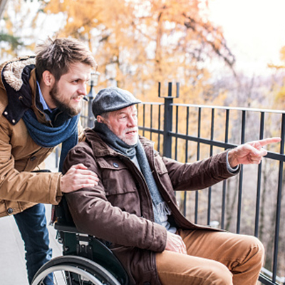 Afbeelding van een man in rolstoel die wordt ondersteund door een verzorger